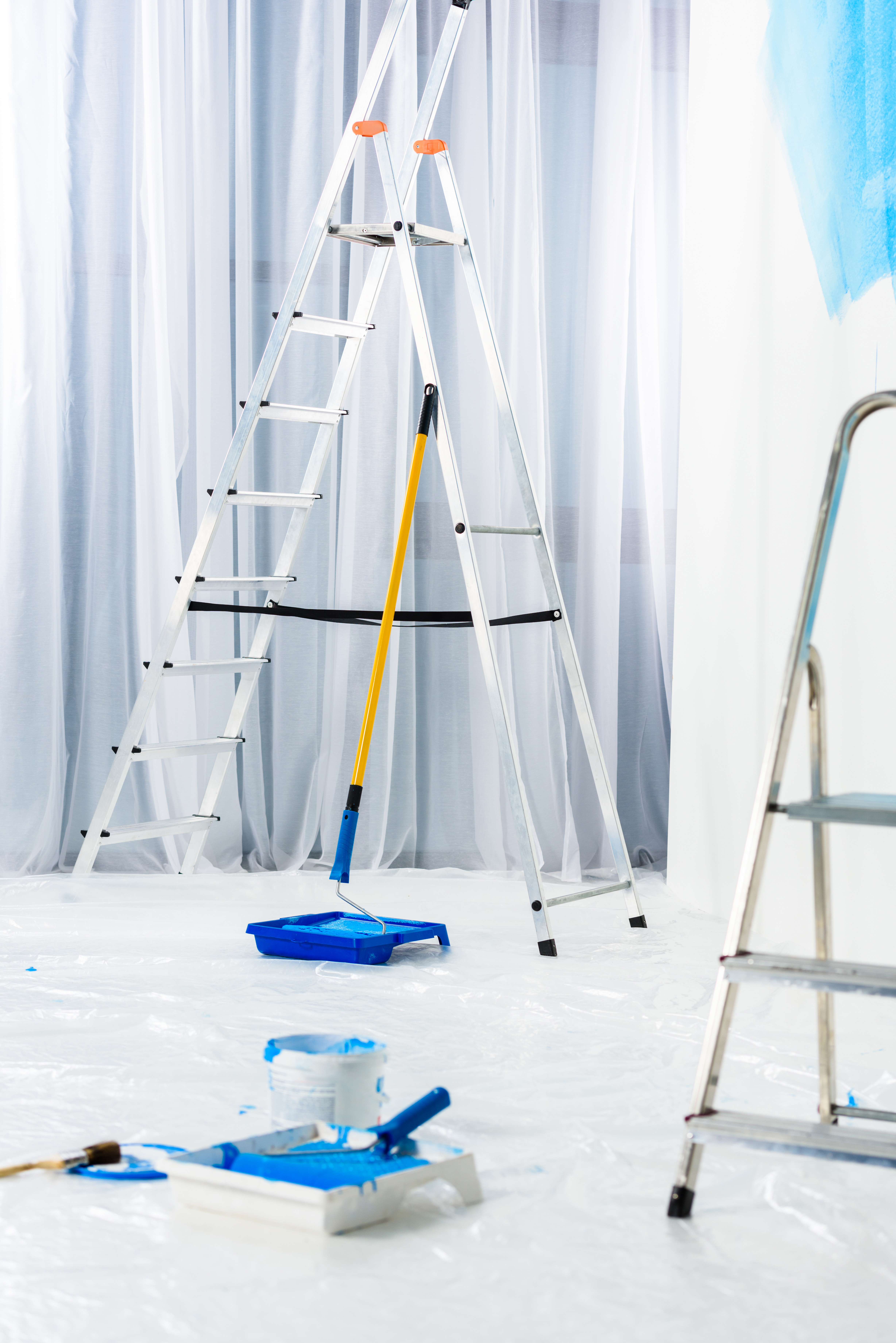 ladders and paint roller brushes in blue paint in room
